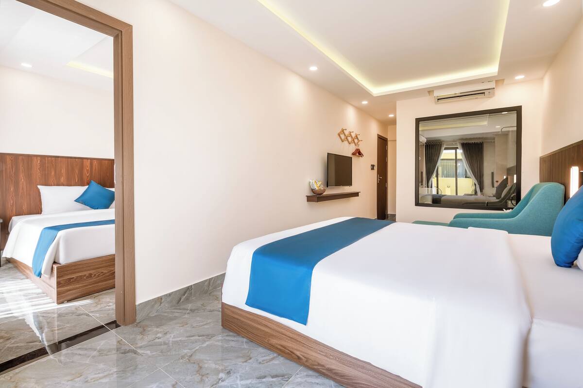A hotel room with two beds, a TV, a mirror, and a seating area.