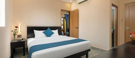 A modern hotel room with a large bed, a nightstand, a desk, and an air conditioning unit.