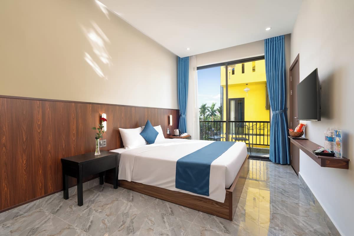 A hotel room with a bed, a nightstand, a TV, and a balcony with yellow walls and blue curtains.