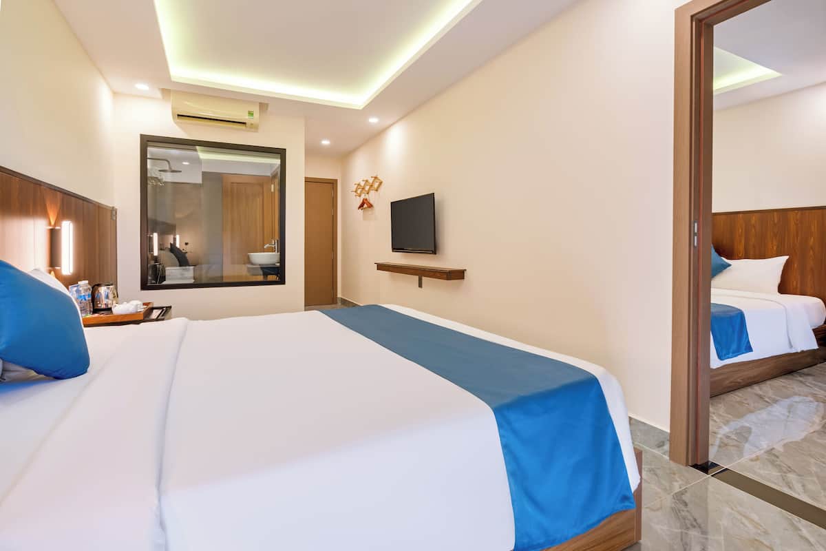 Habitación de hotel con una cama grande, televisión, espejo y baño visible a través de la puerta.
