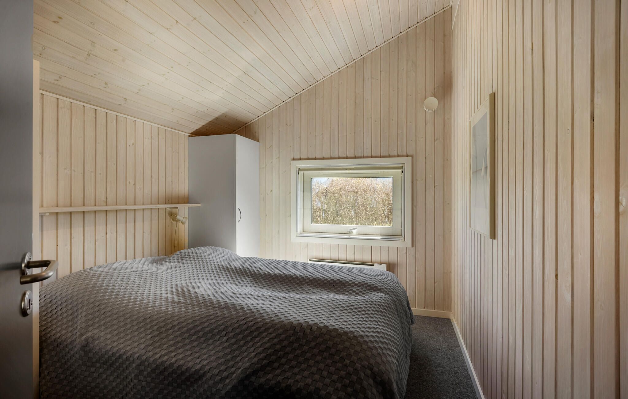 Un dormitorio con una cama, una ventana, paredes de madera y una puerta.