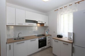 A modern kitchen with white cabinets, a stainless steel sink, a built-in oven, and a refrigerator. - Apartment Samsa (Čižići - island Krk)
