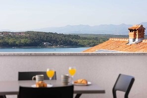 A dining area with a table set for breakfast, overlooking a lake and mountains. - Apartment Boska Soline (Soline)