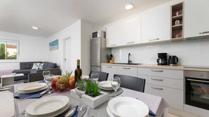 Uma cozinha moderna com armários brancos, forno embutido e área de refeições com mesa posta para quatro pessoas.