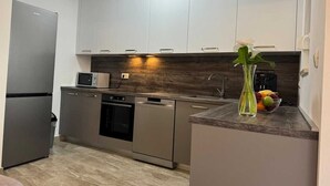 Cozinha moderna com eletrodomésticos de aço inoxidável, armários brancos e painel de madeira.