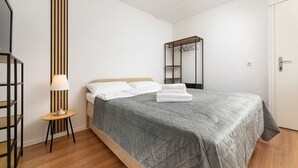 Een keurig opgemaakte slaapkamer met een bed, een nachtkastje met lamp en een garderobe.