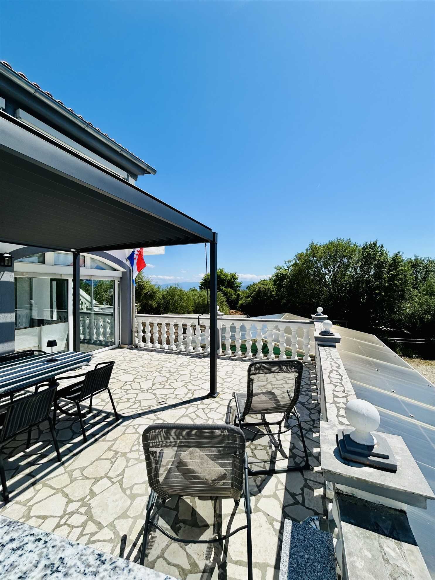 A covered outdoor patio with a table and chairs, a stone floor, and a view of the landscape.