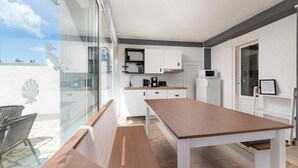A modern kitchen with white cabinets, a wooden table, and a glass sliding door leading to a balcony. - Apartment Maria Zestilac (Žestilac)
