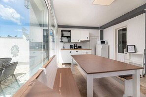 Eine moderne Küche mit weißen Schränken, einem Holztisch und einer Glastür zum Balkon.