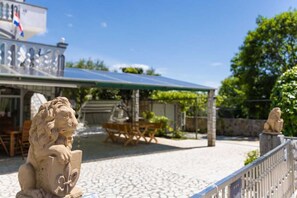 A courtyard with stone lion statues, a covered seating area, and a building with a flag. - Apartment Maria Zestilac (Žestilac)