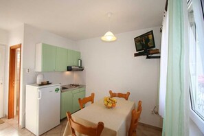 A compact kitchen with a dining table, chairs, a refrigerator, and a television mounted on the wall. - Apartment Dvornicic A4 (Šilo)
