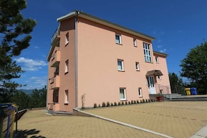 Un edificio a più piani con tetto piatto, un balcone al secondo piano e un cortile lastricato.