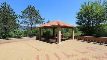 Un gazebo con tetto in tegole, circondato da una zona pavimentata con motivo geometrico.