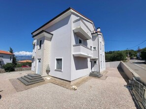 A two-story building with a balcony, a small front entrance, and a gravel driveway.