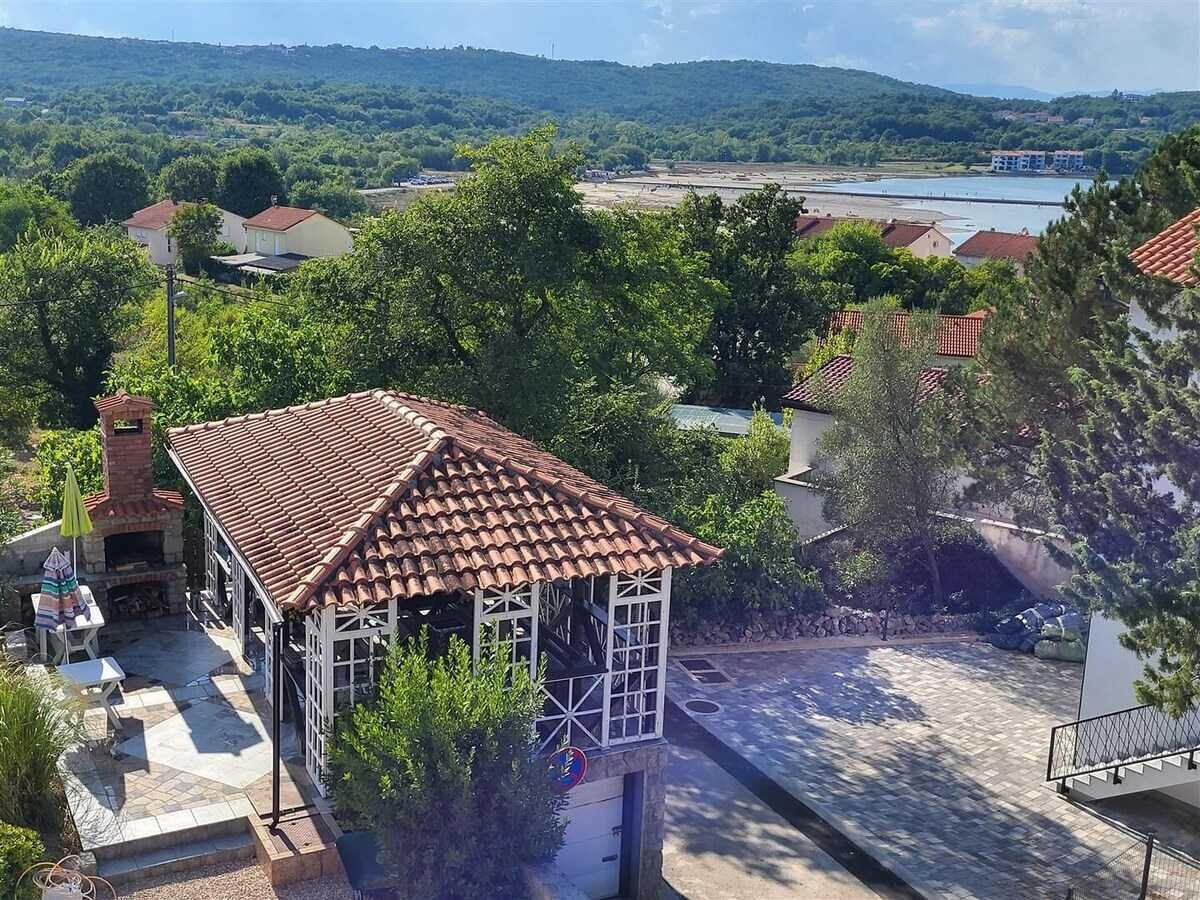 Ein Innenhof mit einem Gebäude mit Ziegeldach, umgeben von Grünflächen und Blick auf ein Gewässer.