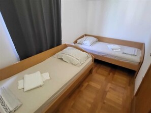 Zwei Einzelbetten mit Holzrahmen und weißer Bettwäsche, ein Holzboden und ein Fenster mit Vorhang.