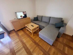 Ein Wohnzimmer mit grauem Sofa, einem Holzschrank und einem Fernseher auf einem Lowboard.