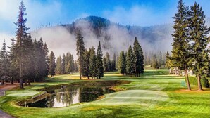 A golf course with a pond, trees, and a mountain in the background.