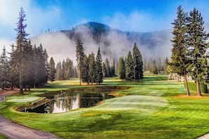 A golf course with a pond, trees, and a mountain in the background.