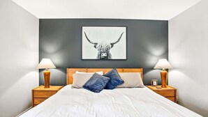 A bedroom with a bed, two bedside tables, lamps, a wall-mounted artwork of a bull, and a dark-colored wall.