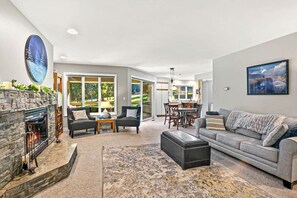 A spacious living area with a fireplace, a sofa, a dining table, and a large window offering a view of the outdoors.