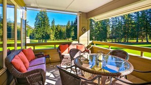 A covered patio with wicker furniture, a glass table, and a view of a golf course.