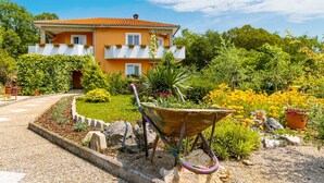 Uma casa de dois andares com jardim, um carrinho de mão e um caminho que leva à entrada.