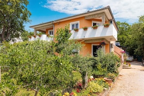 Ein zweistöckiges Haus mit Balkon, umgeben von üppiger Vegetation und einer Schotterauffahrt.