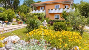 Uma casa de dois andares com um jardim na frente, com flores amarelas e diversas plantas.