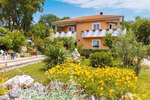 A two-story house with a garden in front, featuring yellow flowers and a variety of plants. - Apartment Adela bijeli (Polje)