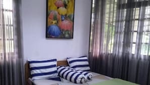 Una cama individual con almohadillas a rayas, una manta verde y un cuadro de paraguas de colores en la pared.