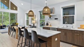 Una cocina moderna con una isla grande, taburetes de bar, luces colgantes y vistas al exterior.