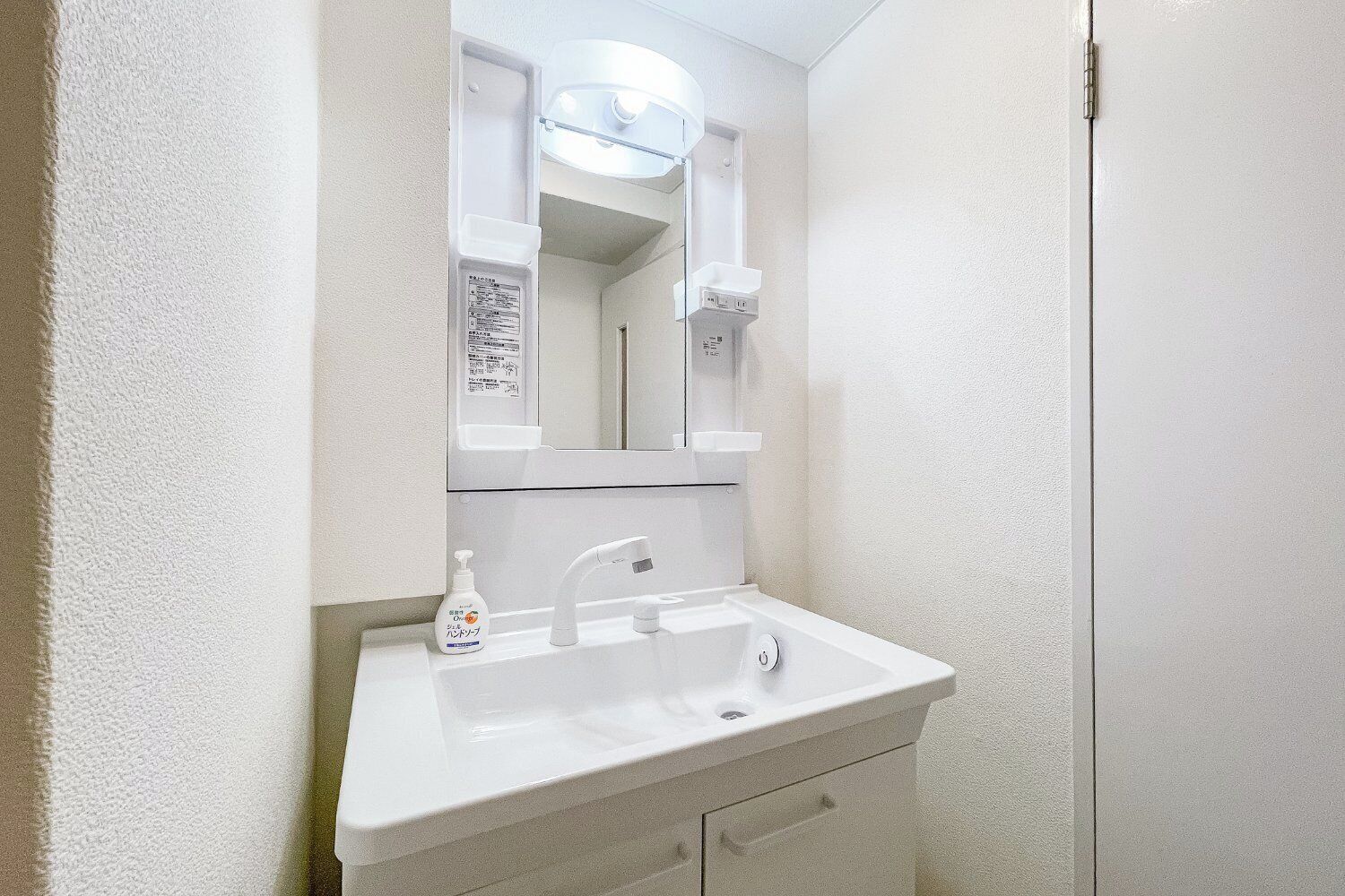 Un baño con lavamanos blanco, espejo y jabón para manos.