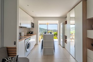 A modern kitchen with a washing machine, a dining area with a view, and a built-in oven. - L'appartement Cala Bianca (BORMES LES MIMOSAS)
