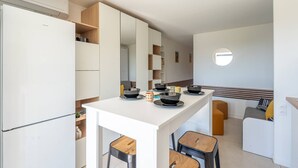 A compact kitchen with white cabinetry, a central island, and a small dining area with stools. - L'appartement Cala Bianca (BORMES LES MIMOSAS)