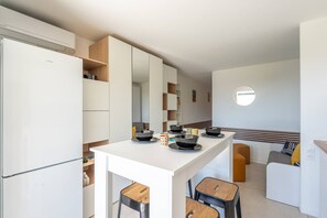 A compact kitchen with white cabinetry, a central island, and a small dining area with stools. - L'appartement Cala Bianca (BORMES LES MIMOSAS)