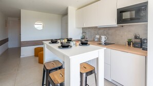 A modern kitchen with white cabinets, a black microwave, and a wooden island with stools. - L'appartement Cala Bianca (BORMES LES MIMOSAS)