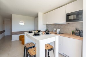 A modern kitchen with white cabinets, a black microwave, and a wooden island with stools. - L'appartement Cala Bianca (BORMES LES MIMOSAS)
