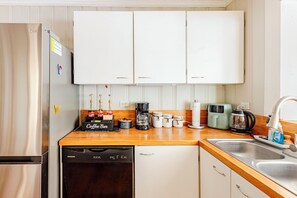 A kitchen with white cabinets, a stainless steel refrigerator, a coffee maker, and a dishwasher. - Thunderbolt Coastal Cottage (Thunderbolt)