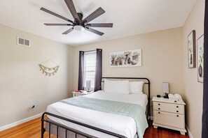 A bedroom with a bed, bedside table, nightstand, wall art, and a ceiling fan. - Thunderbolt Coastal Cottage (Thunderbolt)