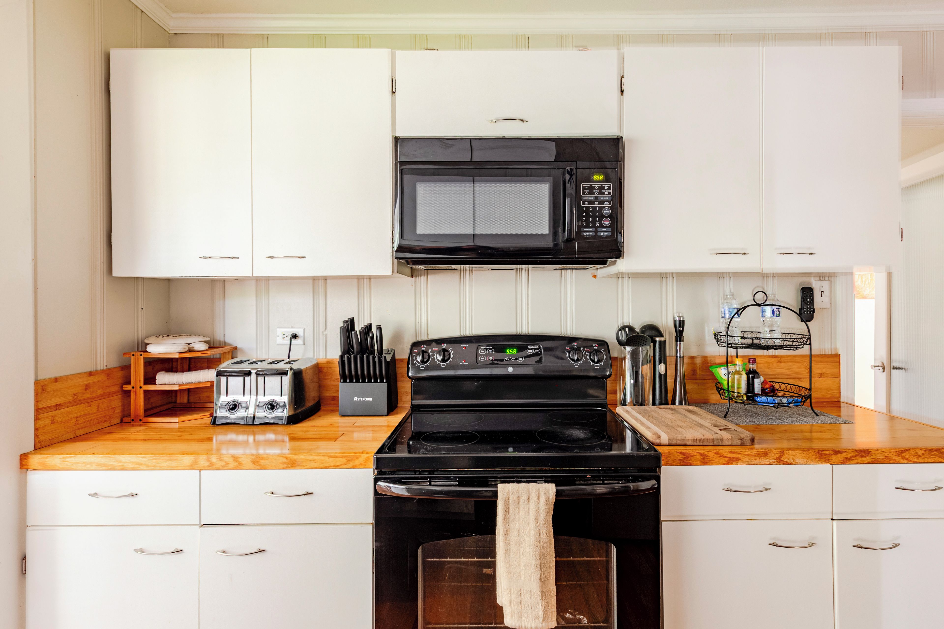A kitchen with white cabinets, a black microwave, a stove, and a toaster.