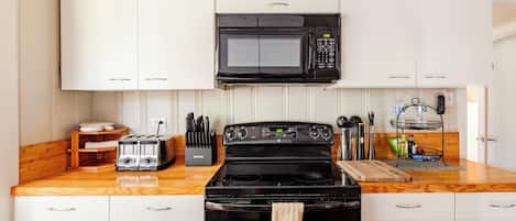 Una cocina con armarios blancos, un microondas negro, una estufa y un tostador.