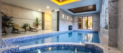 An indoor swimming pool with a tiled edge, wooden ceiling panels, and marble walls.