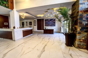 Un vestíbulo de hotel con piso de mármol, un mostrador de recepción, un cuadro grande y una planta en maceta.
