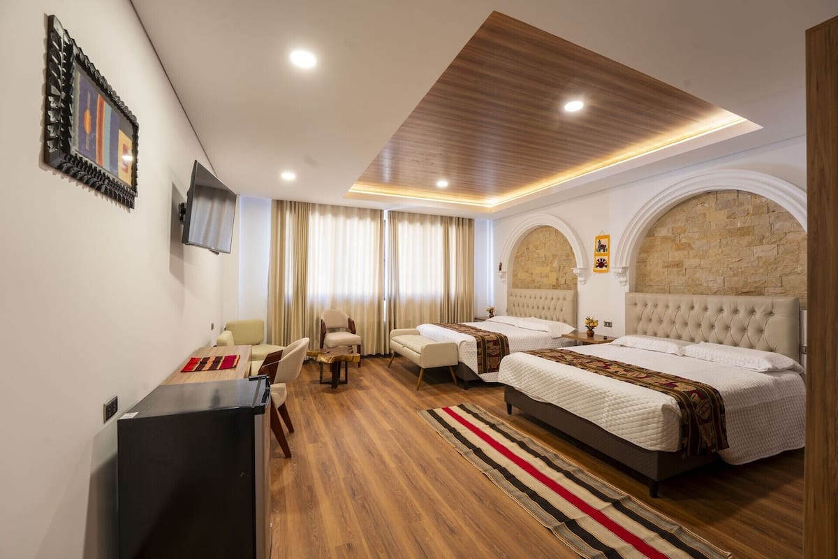 Habitación de hotel con cama, dos sillas, un escritorio, televisor y pared de piedra.