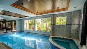 Una piscina con piso y paredes de baldosas, ventanas amplias con vista a follaje y techo de madera.
