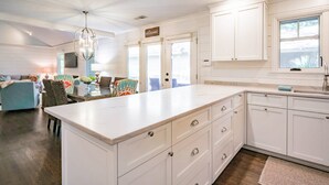 A kitchen with white cabinetry, a marble countertop, and a dining area with colorful chairs. - Slow Down & Reconnect in Renovated, Dog-Friendly Cottage, Four Minutes to Beach w/ Great Back Dec (Kiawah Island)