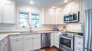 A modern kitchen with white cabinetry, stainless steel appliances, and a window providing natural light. - Slow Down & Reconnect in Renovated, Dog-Friendly Cottage, Four Minutes to Beach w/ Great Back Dec (Kiawah Island)