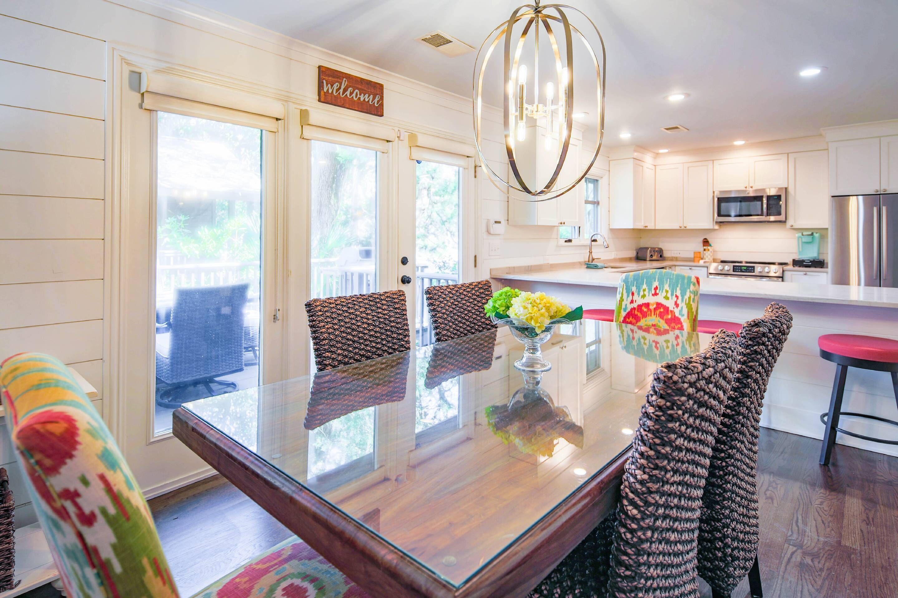 A modern kitchen with white cabinets, a stainless steel refrigerator, and a dining area with a glass table and patterned chairs.