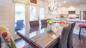 A modern kitchen with white cabinets, a stainless steel refrigerator, and a dining area with a glass table and patterned chairs. - Slow Down & Reconnect in Renovated, Dog-Friendly Cottage, Four Minutes to Beach w/ Great Back Dec (Kiawah Island)